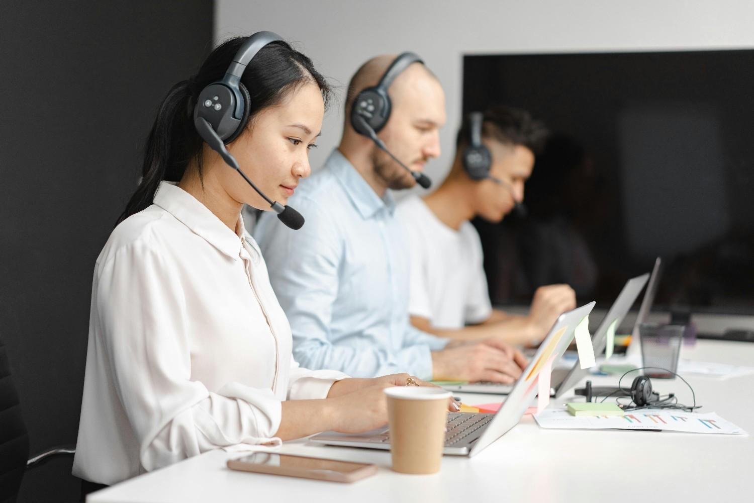 Customer service representatives sitting in a row, wearing headsets and working on laptops