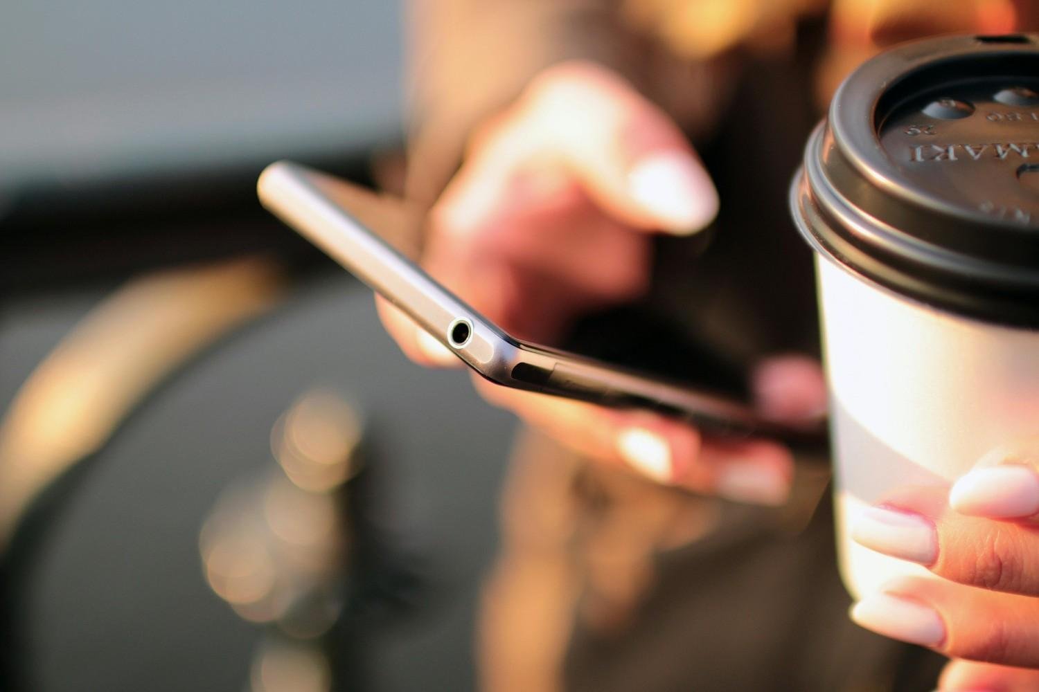 A person holding a phone and a coffee cup