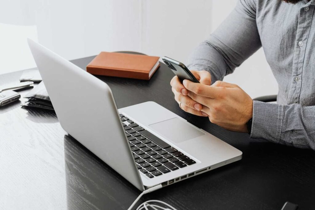 A person using a laptop and phone on top of a table